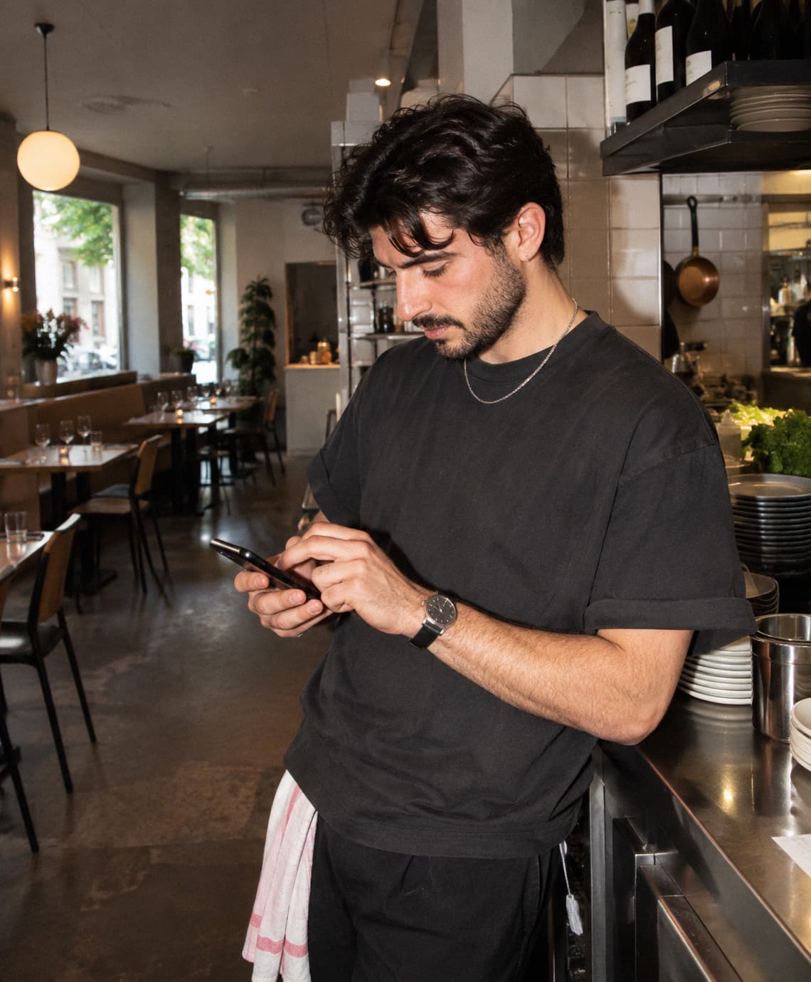 Un restaurateur au passe de la cuisine, en plein service, modifie sa carte sur son téléphone