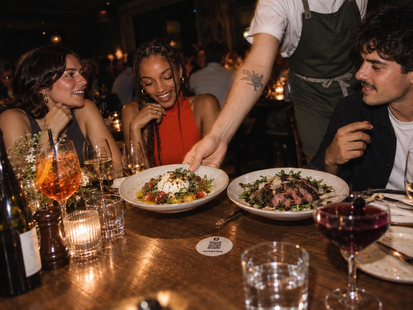 Une tablée d’amis le soir, un serveur pose les assiettes, un sous-verre Swizee sur la table